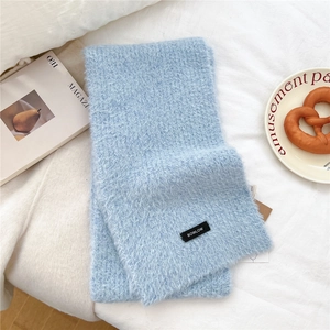 Detail of soft light blue knit scarf with a woven label on cozy white fabric