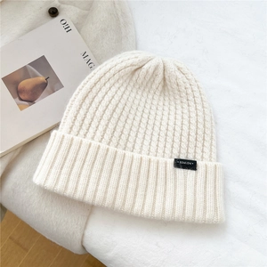 Detailed texture of cream knit beanie with broad folded cuff and black brand label