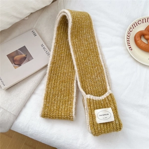 Detailed close-up of a thick mustard yellow knit scarf with white stitched edges and woven label