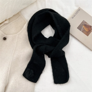 Close-up of black knit scarf with thick fluffy texture and soft pom-pom detail