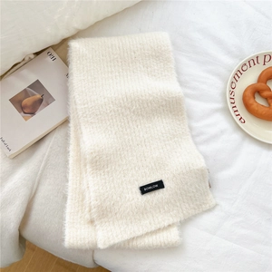 Close-up of cream white wool blend knit scarf with brand label on cozy bed setting