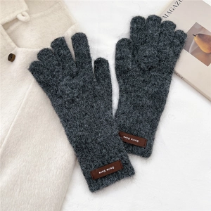 Macro detail of dark grey thick knit gloves with a brown leather label on the wrist