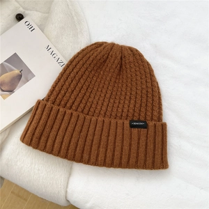 Detailed view of brown wool knit beanie texture with a woven patch on a white background