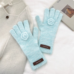 Detail of light blue knit gloves featuring 3D floral accents and a premium leather label