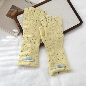 Detail of thick knit gloves in yellow marl texture with a minimalist woven label