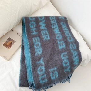 Détail d'une écharpe en tricot gris avec imprimé lettre bleu et franges sur lit blanc