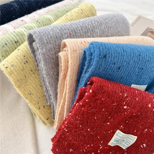 Close-up of thick knitted winter scarves with colorful speckles and woven labels