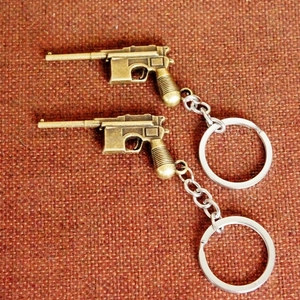 Detail of two vintage bronze metal pistol-shaped keychains on a textured fabric background