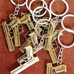 Close-up of bronze metal pistol-shaped keychains with silver rings and engraved warning label
