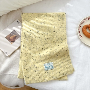 Detail of soft yellow knitted scarf showing warm texture and fabric label on bed