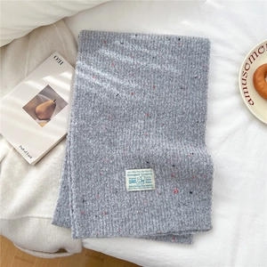 Close-up of grey chunky knit scarf with colorful specks and white woven label detail