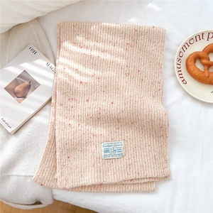 Detailed close-up of chunky knit beige scarf texture with a blue rectangular woven label