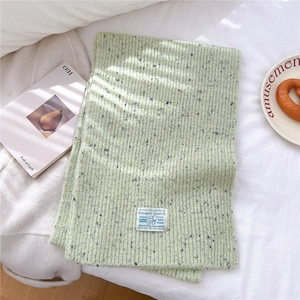 Detail of light green knit scarf showing thick ribbed texture and brand label on white fabric