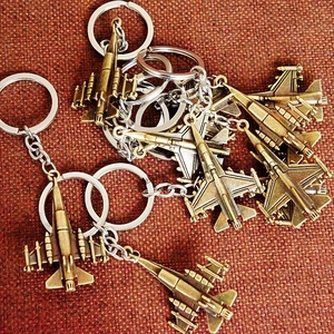 Close-up of bronze metal fighter jet model keychains stacked on red fabric background
