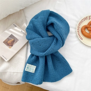 Detail view of blue chunky knit scarf texture with a white woven label on a white background
