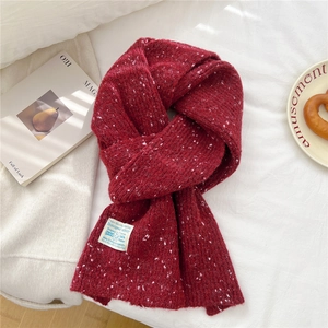 Detail of red knitted scarf with white flecks and branded tag on white bedding