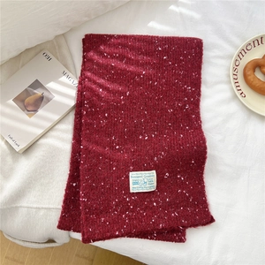 Detail of soft dark red knit scarf with white speckled texture and rectangular label