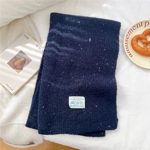 Detail of navy knit scarf with color flecks and woven label on a minimalist background