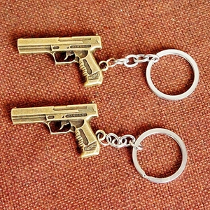 Close-up of bronze pistol-shaped metal keychains with silver rings and detailed engraving