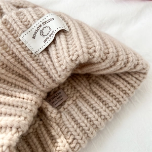 Close-up of beige wool knitted hat showing the woven brand label and 100% wool material