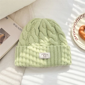 Detail view of thick cable knit texture on a light green 100% wool winter beanie hat