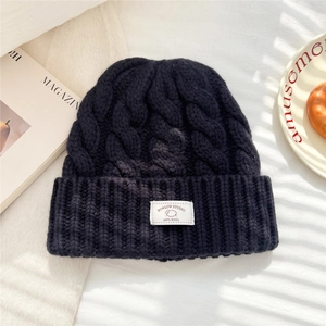 Close-up of cable knit navy blue wool beanie showing thick texture and 100% wool label