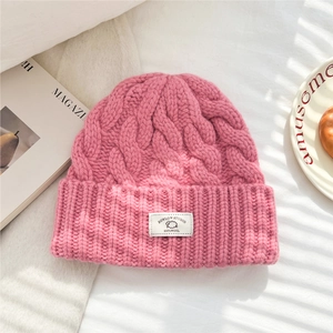 Detail of pink cable-knit wool beanie showing 100% wool label and thick texture
