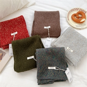 Chunky knit wool scarves in multiple colors with white labels on textured fabric background