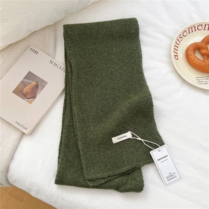 Close-up of dark green wool scarf featuring the 100% wool label and brand tag on white fabric