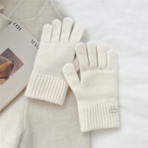 Detailed close-up of cream knit gloves with ribbed cuffs and round metal logo plate