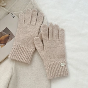 Detailed knit texture of beige wool-like gloves with ribbed cuff and metal brand tag