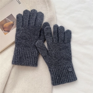 Close-up of dark grey knitted winter gloves with ribbed cuffs on a soft fabric background