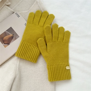 Detail of ginger yellow knitted gloves with ribbed cuffs and decorative metal label