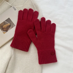 Detail of burgundy knit gloves with ribbed cuffs and leather label on white coat