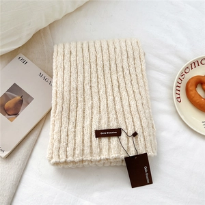 Detail of chunky cream knit scarf featuring vertical rib texture and a brown leather logo tag