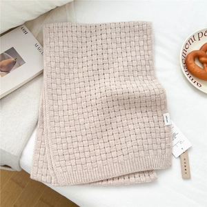 Detailed texture of 100% wool knit scarf with camphor wood anti-moth tag on white bed