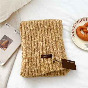 Detailed close-up of thick rib-knit ginger yellow scarf with brand label on white fabric