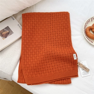 Close-up of orange wool scarf showing waffle weave texture and 100% wool label