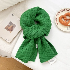 Detailed view of green knitted wool scarf with woven checkered texture and brand label