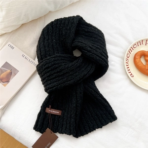 Close-up of black chunky knit scarf featuring a leather brand tag and cozy winter texture
