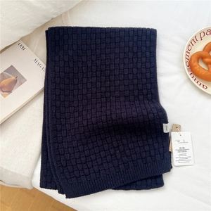 Close-up of dark blue wool knit scarf showing waffled texture and 100% wool label