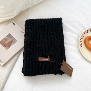 Close-up of black chunky knit scarf featuring a brown leather brand label and soft texture