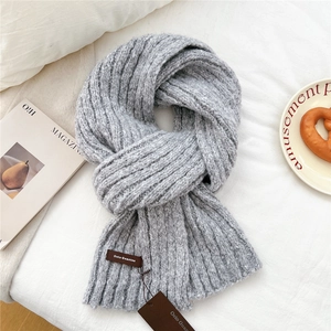 Detail of grey chunky knit scarf texture with a brown leather logo tag on white bedding