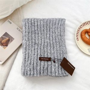 Detail of thick grey knit scarf with leather brand label on soft white fabric