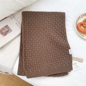 Detail of a brown 100% wool knitted scarf showing waffle texture and brand tag on bed