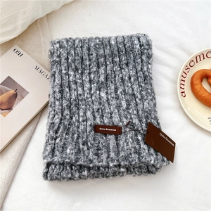 Detail shot of a thick grey knit scarf with a brown leather label on white fabric