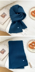 Close-up of teal wool knit scarf with vertical ribbed texture and brand wooden tag