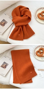 Detailed texture of orange knitted wool scarf featuring chunky vertical ribbed weave and tags