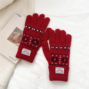 Close-up of red knit gloves with snowflake patterns and ribbed cuffs on white fabric