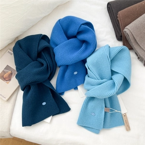 Trio of blue ribbed wool scarves with branded buckle on a soft white fabric background